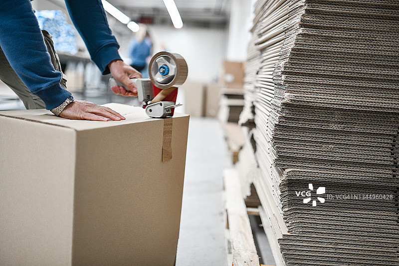 纺织厂仓库中男工人在箱子上贴胶带图片素材