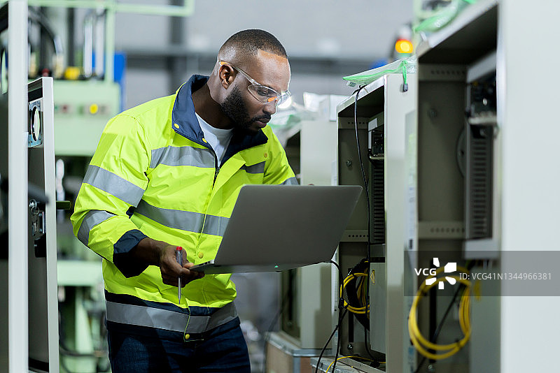 非裔美国工程师手持笔记本电脑，检查制造系统，智能技术员输入NC数据程序，控制汽车行业的数控机床图片素材