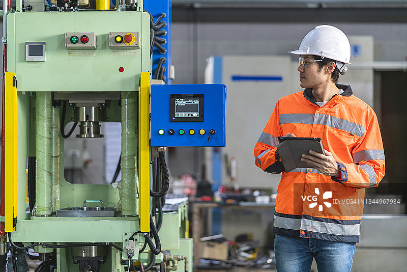 亚洲男性工程师手持笔记本电脑，检查制造系统的运行过程，智能技术人员输入NC数据程序，在汽车工业中控制数控机床图片素材