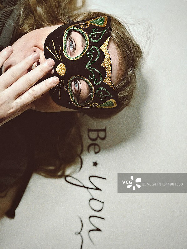 戴着猫面具的可爱少女，微笑并躺在“做你自己”的标志上图片素材