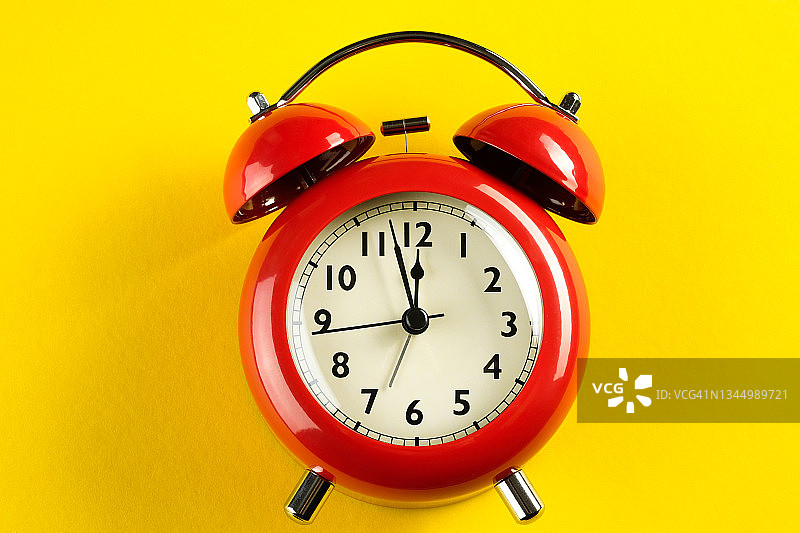 明亮黄色背景上的红色复古闹钟：时间流逝的概念图片素材