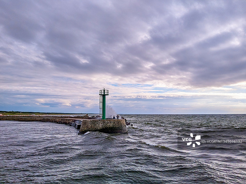 游客站在灯塔旁，观看波罗的海海浪冲击达尔沃/达尔武科港的西侧防波堤，该防波堤分隔了波罗的海和维普扎河图片素材