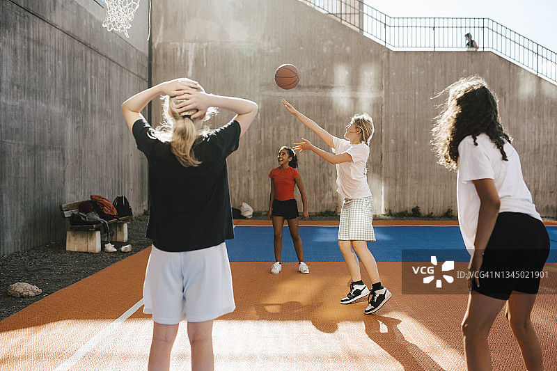 在球场上和朋友们一起玩耍，将篮球投向篮筐的女孩图片素材