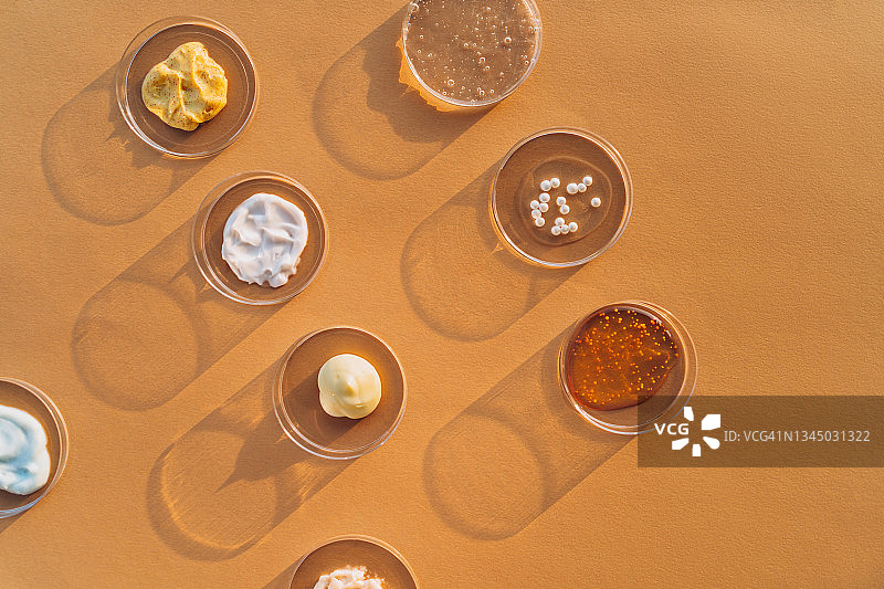 米色背景下的培养皿中盛放的彩色乳霜、磨砂膏、面部精华和凝胶，化妆品实验室研究概念，扁平风格摄影，含文案空间图片素材