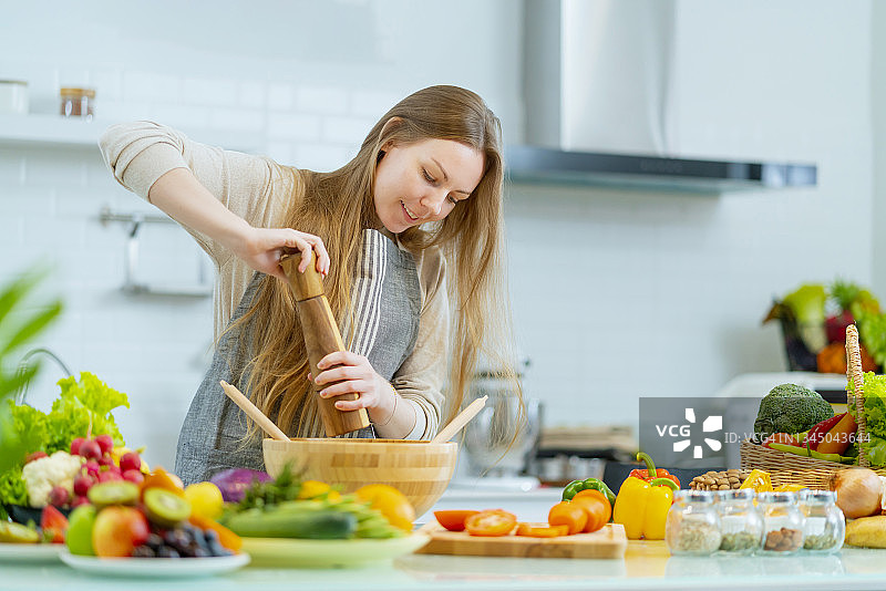 白人家庭主妇在厨房准备自制沙拉，单身女士在餐桌旁拿着刀切新鲜的天然辣椒和番茄，准备蔬菜沙拉图片素材