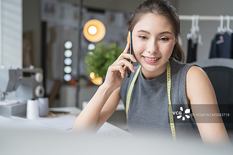 专业女时装设计师在工作室用手机交谈图片素材