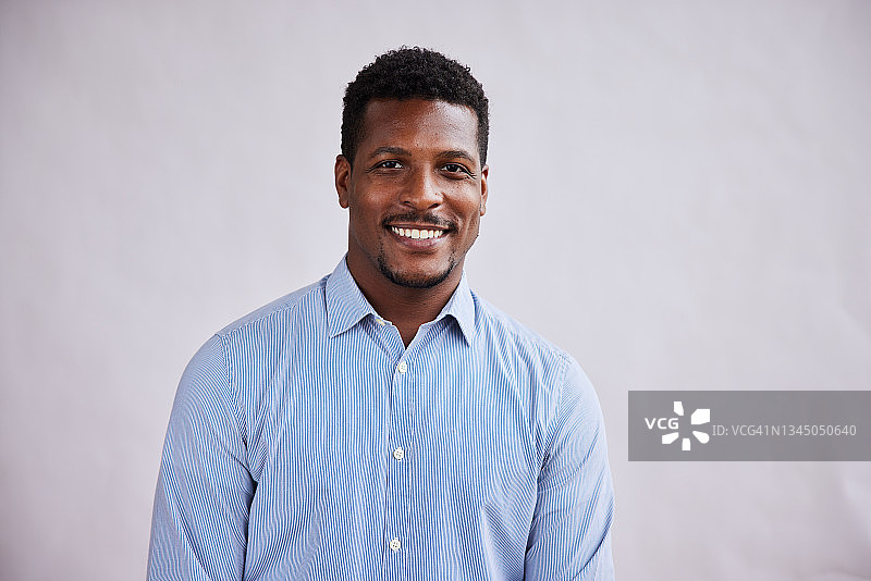 自信的年轻商人灰色背景前微笑图片素材