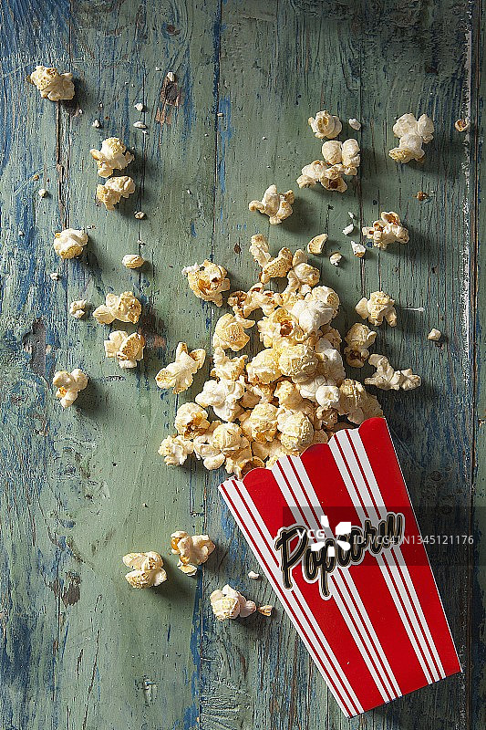 盒装爆米花洒落于水蓝色木板上图片素材