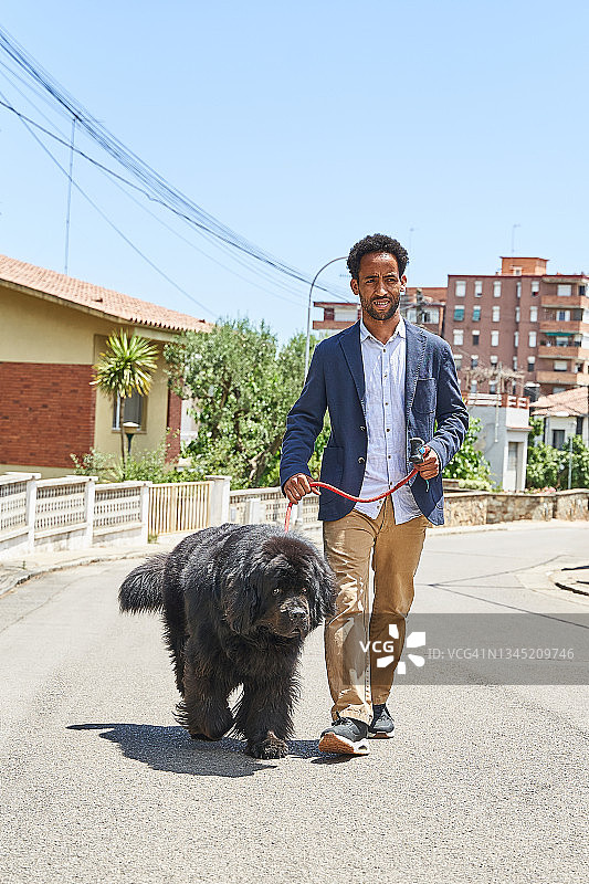 男人带着黑狗在蔚蓝天空下行走图片素材