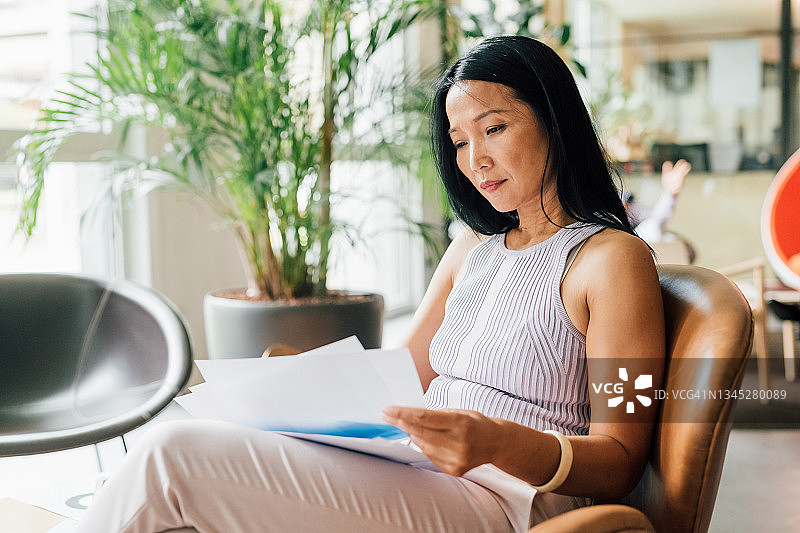 意大利：女子坐在扶手椅上，在创意工作室阅读文件图片素材