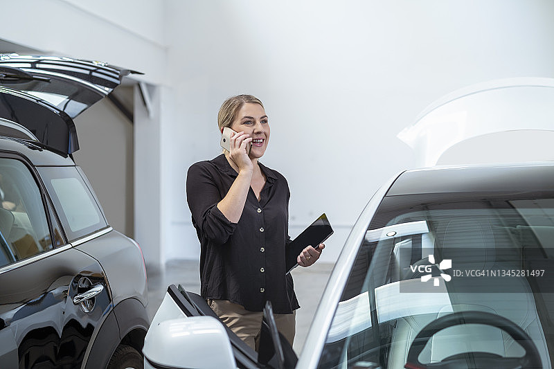 在停车场里，女人在她的车旁用智能手机交谈图片素材