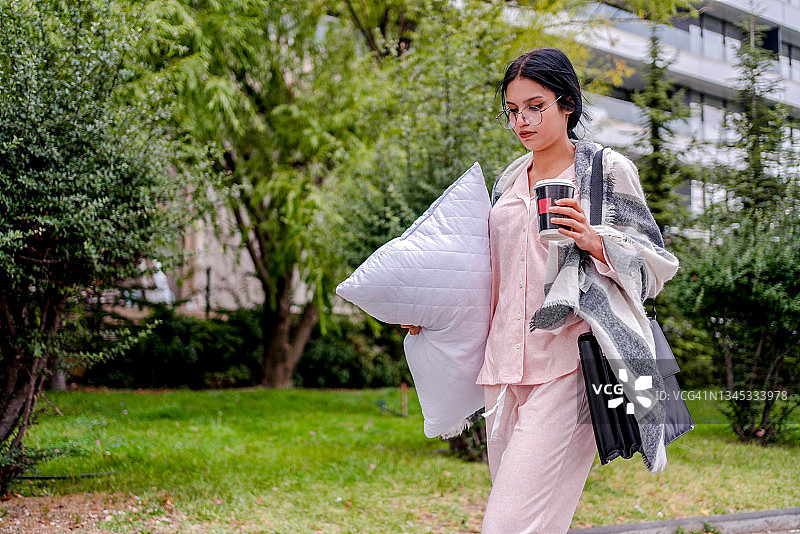 穿着睡衣和拖鞋，手持枕头行走的女商人图片素材