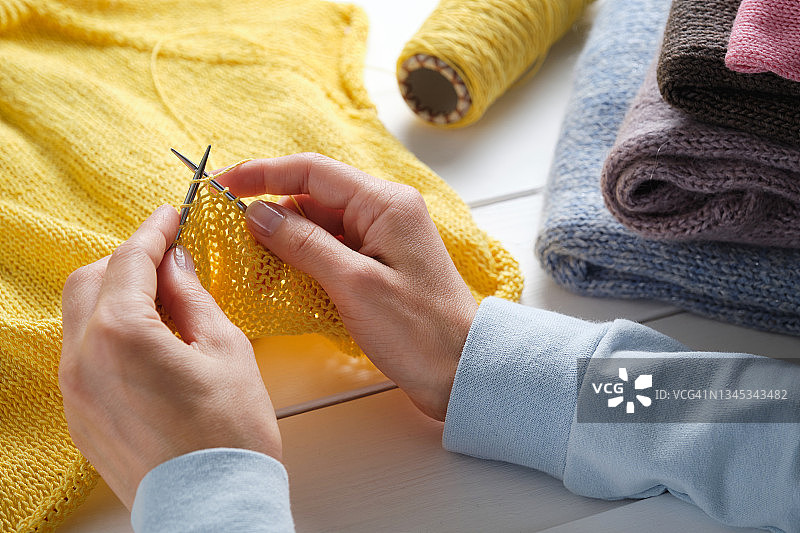 一名女子在白色木桌背景上用棉线和羊毛纱线编织。旁边放着一团线和一堆衣服。创意工作和生活、爱好概念。用自己的双手制作衣服图片素材