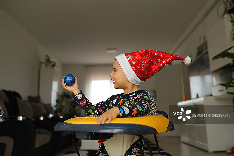 在学步车里的好奇幼儿男孩玩着圣诞装饰品图片素材