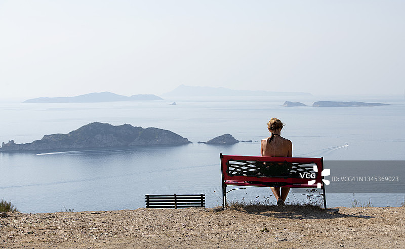 女子背影，坐在希腊科孚岛阿菲奥纳斯附近的海滩长椅上图片素材