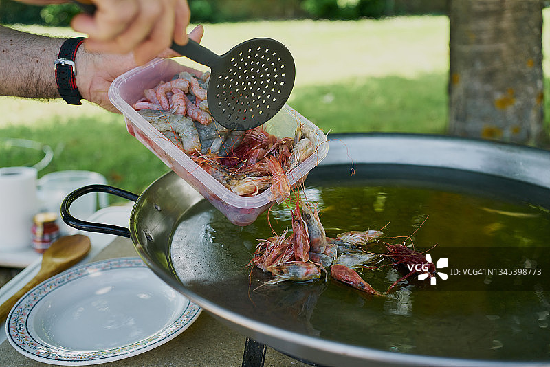 一名男子将小龙虾的头放入装有水的平底锅中，准备在后院用高汤制作海鲜饭图片素材