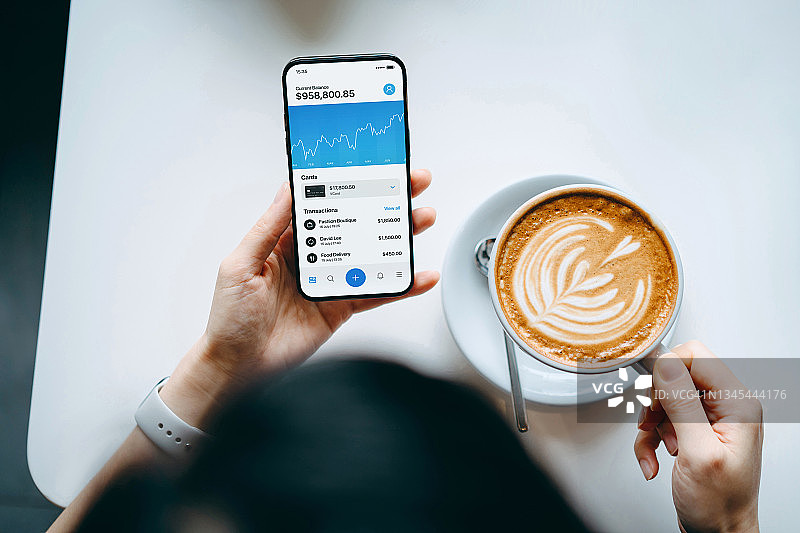 年轻女性在咖啡馆享受咖啡，用手机查看金融股票市场数据，管理财务和投资图片素材