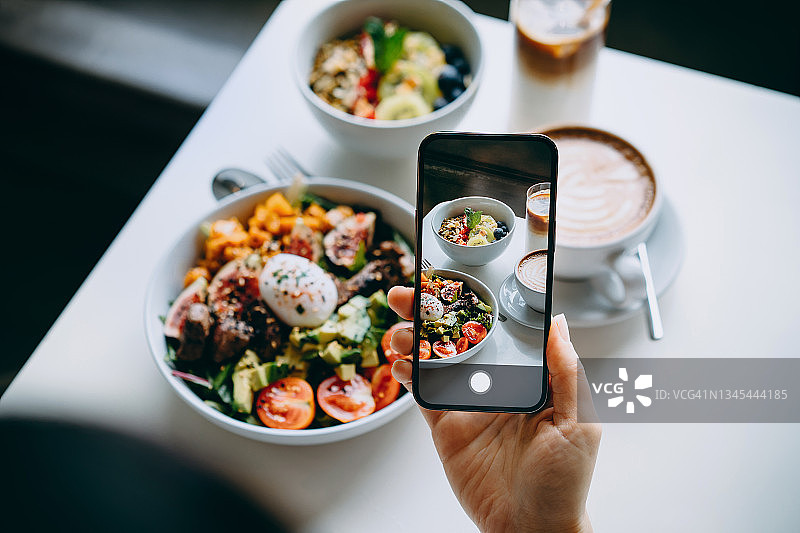 女人在咖啡馆用餐前用智能手机拍摄美味的牛肉沙拉和燕麦水果碗图片素材