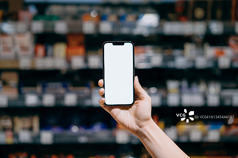 在超市购物时手持智能手机的视角，屏幕空白样机图片素材