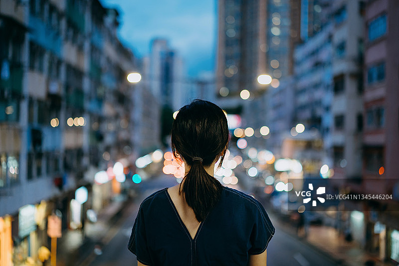 年轻亚洲女子站在黄昏时分灯火通明的城市街道上的背影图片素材