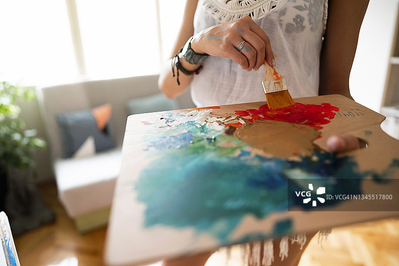 身份不明的女艺术家用画笔在木制调色板上调和油彩图片素材