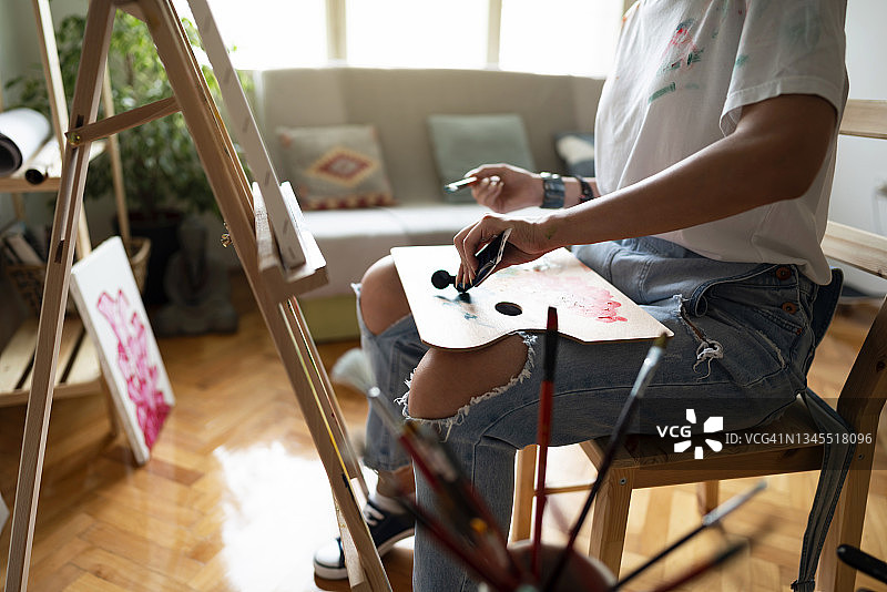在她的艺术工作室里，一位不知名的女艺术家正在艺术家调色板上挤压颜料管中的颜料图片素材