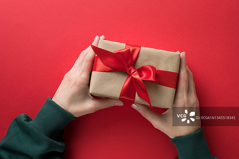 穿着绿色毛衣的女孩在红色背景下拿着一个用明亮丝带系着的精美礼品盒。圣诞节、生日、情人节概念图片素材
