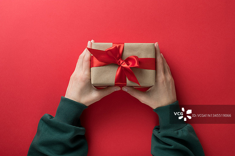 穿着绿色毛衣的女孩在红色背景下拿着一个用明亮丝带系着的精美礼品盒。圣诞节、生日、情人节概念图片素材