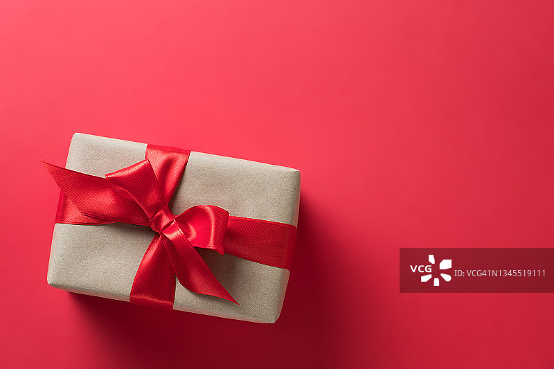 礼品盒、包裹，用牛皮纸包裹并系着鲜艳丝带的惊喜，在红色背景上。节日前夕赠送礼物。圣诞节、情人节、生日的概念。留白图片素材