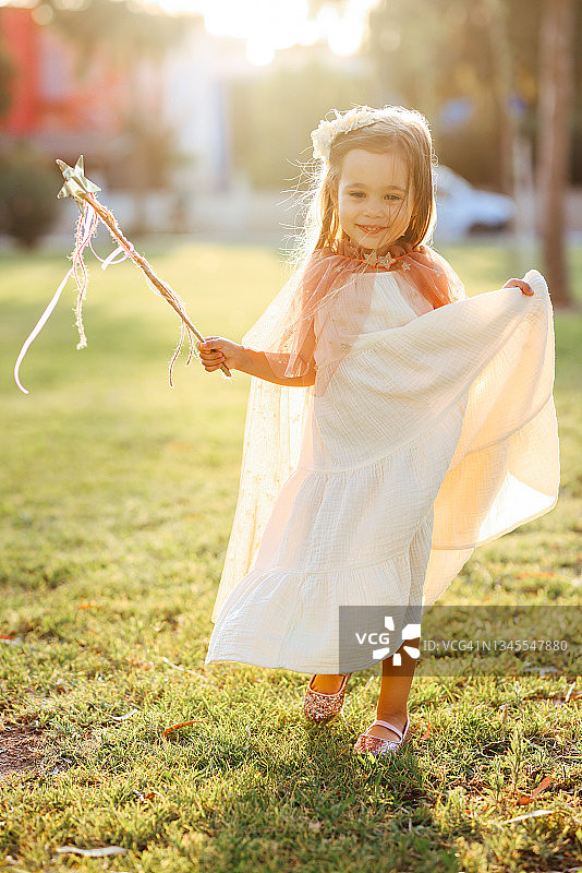 穿着仙女服装的小女孩在绿草地上拿着魔杖跳跃图片素材