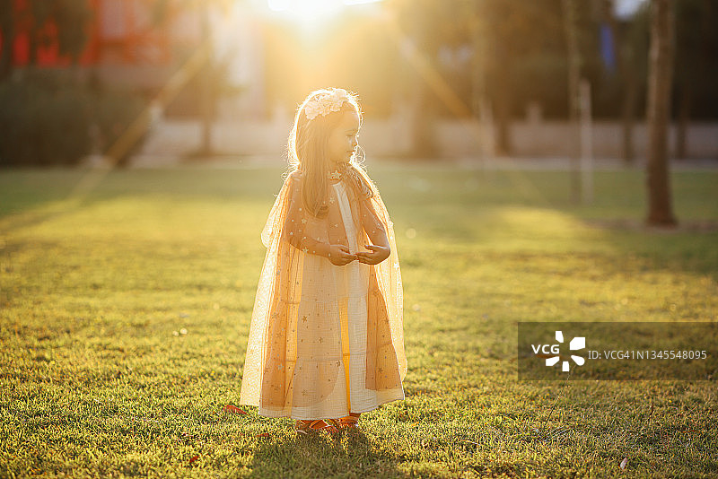 穿着仙女服装的小女孩在绿草地上拿着魔杖跳跃图片素材