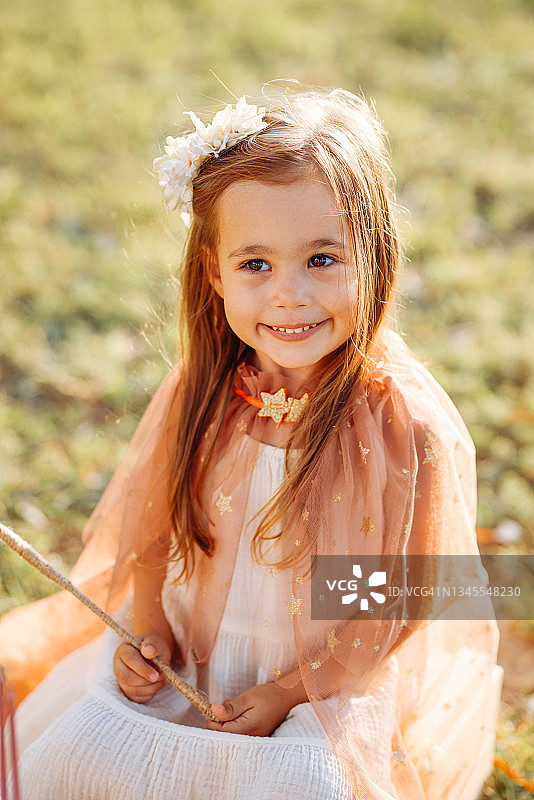 穿着仙女服装的小女孩在绿草地上拿着魔杖跳跃图片素材