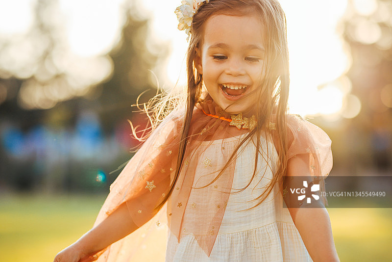 穿着仙女服装的小女孩在绿草地上拿着魔杖跳跃图片素材