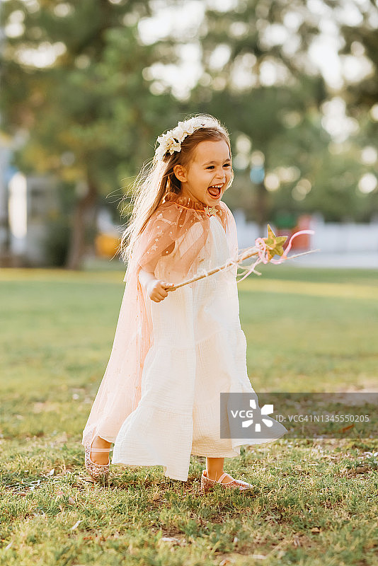 穿着仙女服装的小女孩在绿草地上拿着魔杖跳跃图片素材