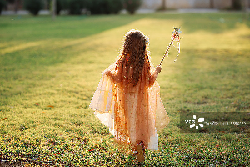 穿着仙女服装的小女孩在绿草地上拿着魔杖跳跃图片素材
