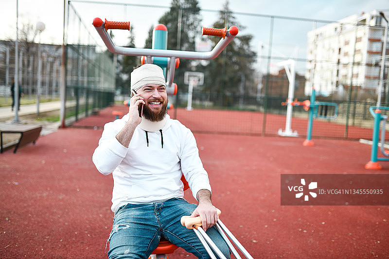 微笑的络腮胡男人在户外受伤后享受电话交谈图片素材