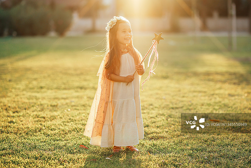 穿着仙女服装的小女孩在绿草地上拿着魔杖跳跃图片素材