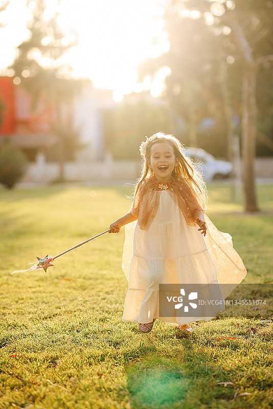 穿着仙女服装的小女孩在绿草地上拿着魔杖跳跃图片素材