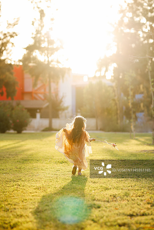 穿着仙女服装的小女孩在绿草地上拿着魔杖跳跃图片素材