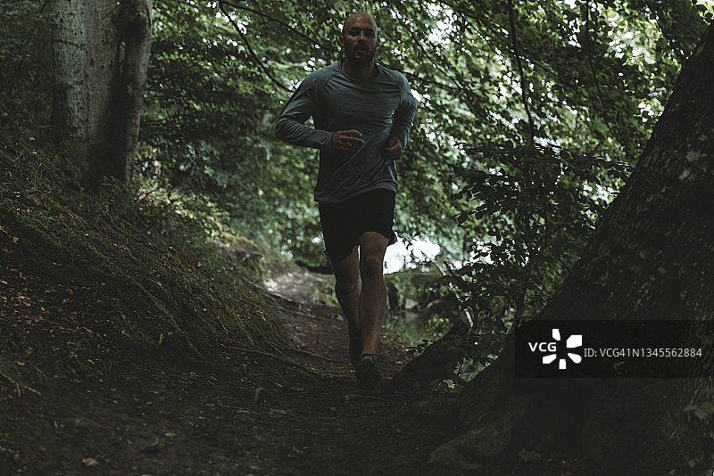 在绿色森林中佩戴智能手表的越野跑者图片素材