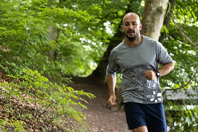 在绿色森林中佩戴智能手表的越野跑者图片素材