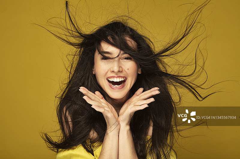 年轻女子脸颊上有痣，头发飞扬，开心地笑着图片素材