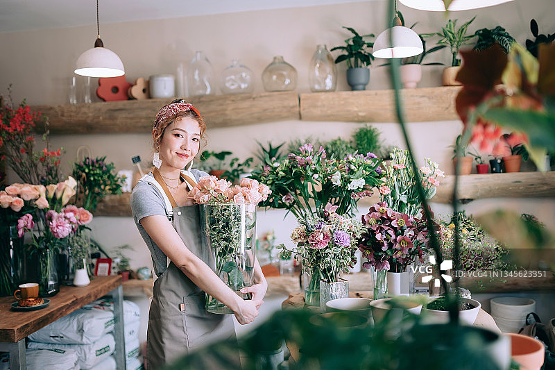 自信的年轻亚洲女花店主肖像，手捧玫瑰花束站在花店里，面带微笑看着镜头，享受与花为伴的工作，小企业概念图片素材