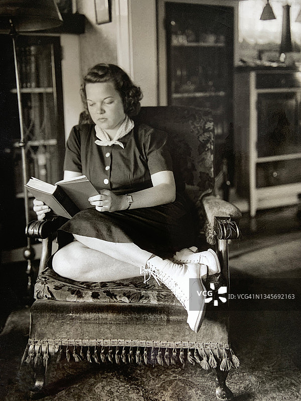 1940年黑白照片：坐在椅子上阅读的年轻女子图片素材
