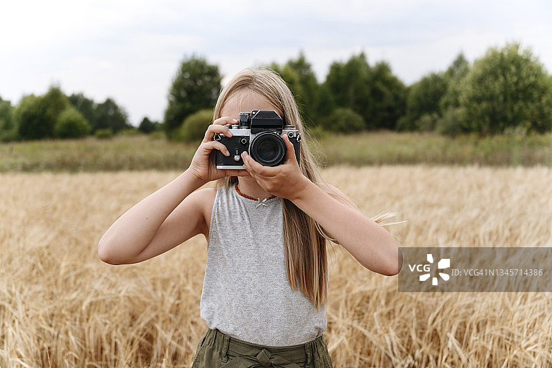 金发女孩在麦田里用相机拍照图片素材