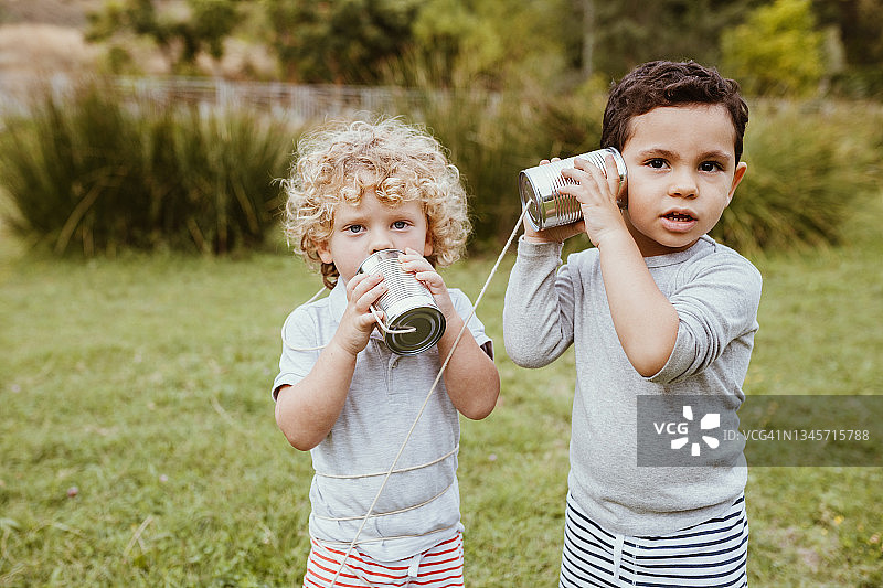 在草地上用罐头电话交流的可爱男孩们图片素材