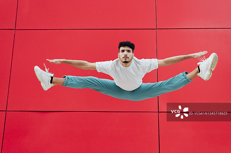 在红墙前伸展双臂劈叉的男人图片素材