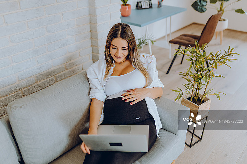 在家享受怀孕、使用笔记本电脑和听音乐的美丽女人图片素材