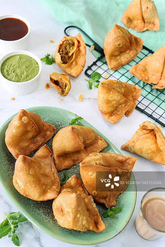 炸三角饺绿色盘子照片：土豆、豌豆和肉馅，冷却架，绿色棉布，薄荷香菜酱和芒果酸辣酱，奶茶，大理石背景图片素材