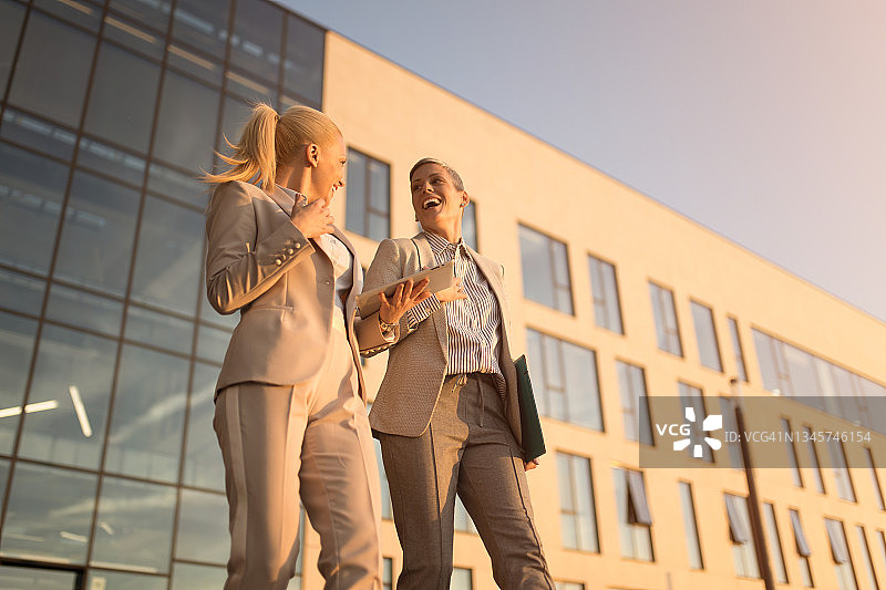 两位快乐的女商人在离开办公大楼时进行讨论。图片素材